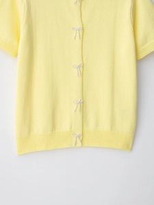 Detail of light yellow short sleeve knit cardigan with white pearl bow accents