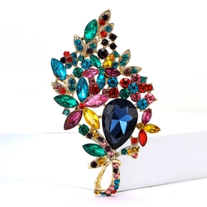 Detail of vintage gold alloy brooch with a large teardrop blue crystal and colorful rhinestones