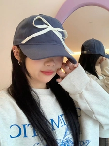Close-up of navy baseball cap featuring a white ribbon bow and adjustable strap detail