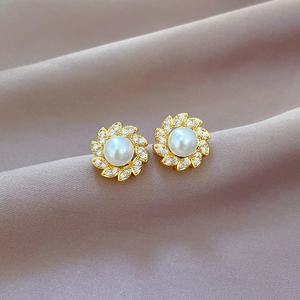 Detailed macro view of gold floral pearl earrings with clear zircon stones on silk fabric