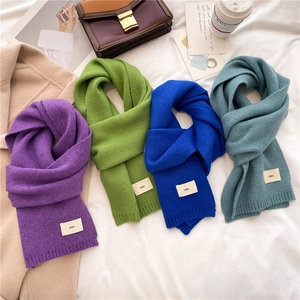 Knitted winter scarves in purple, green, and blue displayed on a soft white bed sheet