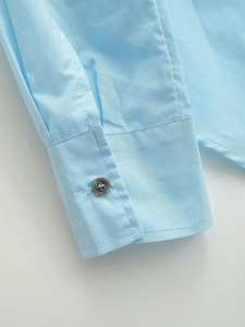 Close-up of light blue cotton shirt cuff showing pleat details and a dark brown button