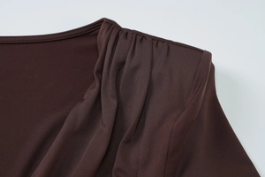 Close-up of pleated detail on dark brown slim-fit long-sleeved dress fabric texture