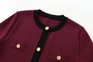 Detail of burgundy knit cardigan with contrast black trim and embossed gold metal buttons