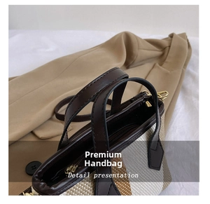 Detail of the brown leather handle and zipper on the striped woven crossbody handbag