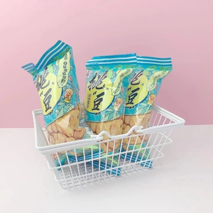 Mini white wire basket storing packs of roasted broad bean snacks on a pink background