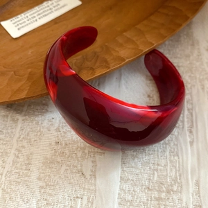 Close-up of a retro red marble-textured acrylic chunky bangle on a wooden tray