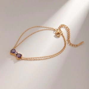 Detailed close-up of a double-layered 18k gold-plated bracelet with purple zircon bow