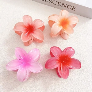 Top view of four gradient plumeria hair claws in pink and orange acrylic on white background