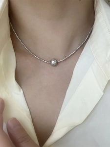 Close-up of a minimalist silver beaded necklace with a central pearl-shaped bead pendant