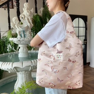 Detail of pink satin tote bag featuring colorful butterfly embroidery and logo patch