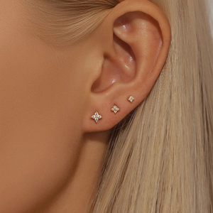 Three sizes of gold flower stud earrings with zircons shown on a model's ear