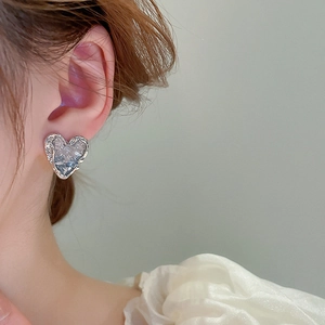 Detail of silver heart-shaped stud earrings with hammered metal texture and blue-grey inlay