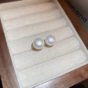 Detailed view of high-quality round white pearl earrings in a luxury wood jewelry box
