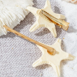 Detail of beige starfish hair clips with gold alligator and snap clip on sand texture