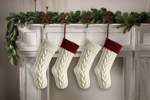 Detailed cable knit Christmas stockings hanging on a fireplace with festive pine garland