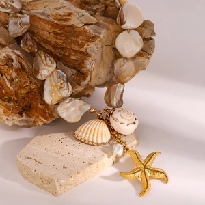 Detailed close-up of shell necklace with golden starfish and pearl on a natural stone