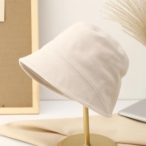 Minimalist beige cotton-linen bucket hat displayed on a modern gold stand