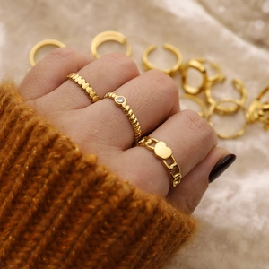Close-up of three 18K gold-plated stainless steel rings worn on soft beige fabric