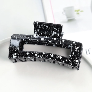 Rectangle black hair claw clip with white ink splatter pattern on a lifestyle setting