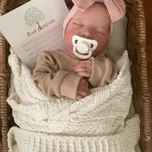 Lifelike sleeping reborn doll Levi in brown sweater and knitted blanket in woven basket