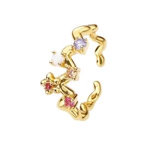 Bague ouverte dorée ondulée ornée de zircons multicolores sur un fond blanc épuré