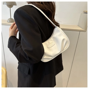 Gros plan d'un sac demi-lune en cuir blanc porté avec un blazer noir par un mannequin