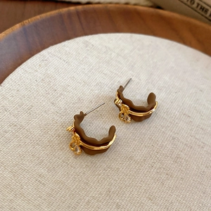 Detail of C-shaped resin earrings in brown and gold with cubic zirconia on a tray