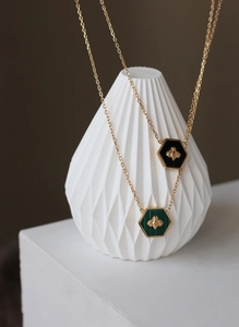 Detail of 18K gold-plated hexagonal necklaces featuring bee charms with black and green inlay
