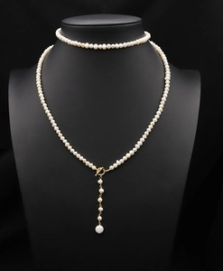 Detail of natural cream pearl sweater chain with gold T-bar clasp on model