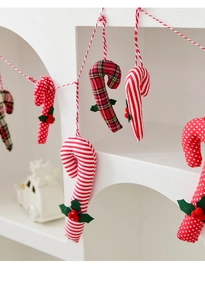Detail of fabric candy cane ornaments with red berries and holly leaves on a festive string