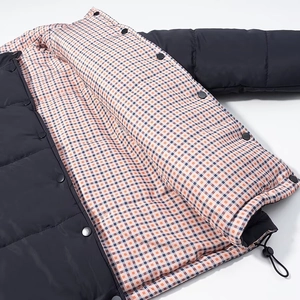 Detail of snap button closure and drawstring hem on a black quilted jacket with plaid lining