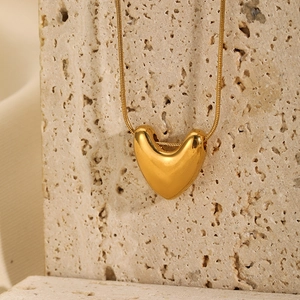 Detail of a polished gold heart pendant necklace hanging on textured beige stone