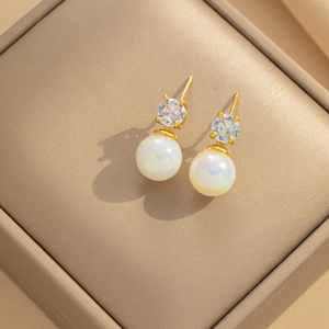 Elegant gold earrings with sparkling zircon and iridescent pearl in a luxury jewelry box