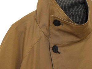 Detail of tan trench coat collar with twill texture, striped lining and black button