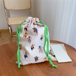 Detail of cotton drawstring bag with cartoon bear prints and green woven cords on wood
