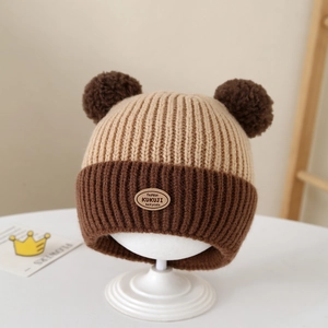 Detail of baby knitted hat featuring double pom-poms and a leather fashion patch