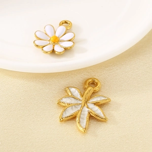 Detail of 18K gold-plated daisy and palm leaf pendants on white ceramic and silk