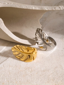 Detailed view of monstera leaf ring in gold and silver finish on textured sand background