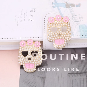 Exaggerated skull earrings with white pearls, pink enamel flowers and heart cut-outs