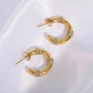 Boucles d'oreilles créoles dorées en C avec zircons micro-pavés sur satin blanc