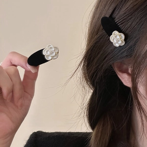 Elegant black velvet camellia hair clips with pearl details shown on hand and worn on hair