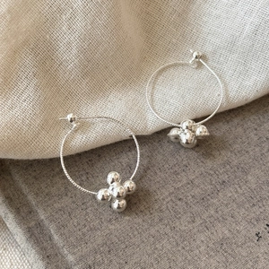 Detail view of silver geometric hoop earrings with five-ball cluster floral drop charms