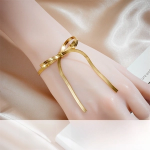 Detail of gold-plated stainless steel bow bracelet with snake chain texture on silk