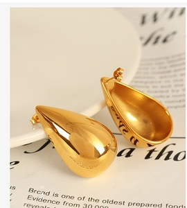 Macro shot of polished gold water drop earrings resting on a white ceramic plate