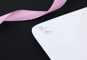 Macro shot of S925 sterling silver freshwater pearl earrings on white tray with pink ribbon