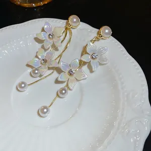 Elegant gold earrings with iridescent flowers, pearls and tassels on white porcelain