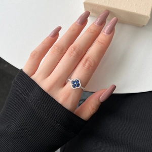 Detailed view of silver ring featuring blue stone clover and sparkling zircon on a hand