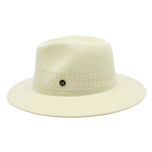 Détail d'un chapeau panama beige avec motifs ajourés et badge métallique doré lettre M