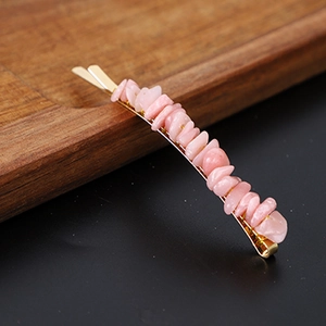 Macro shot of natural pink crystal chips on a golden metal hairpin against wood